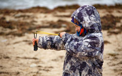 A boy in a jacket on the sand shoots with best slingshot ammo