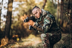 Camouflage soldier with rifle and painted face playing airsoft outdoors in the forest