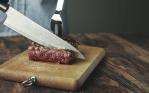 Knife cut slice of grilled meat on wooden board