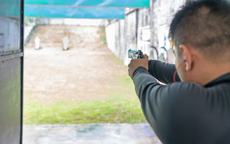 Rear view of a man shooting with gun at target in shooting range