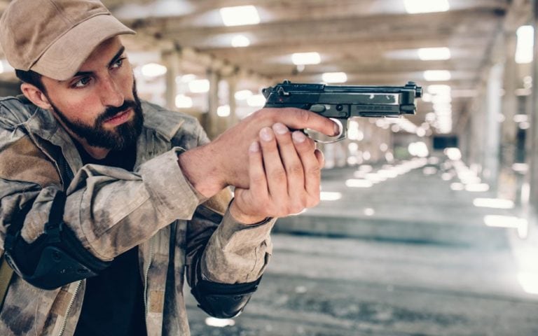 Serious man is standing in hangar and holding airsoft gun in hands