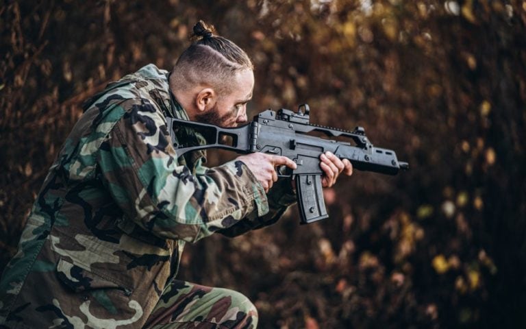 soldier with rifle and painted face playing airsoft outdoors in the forest