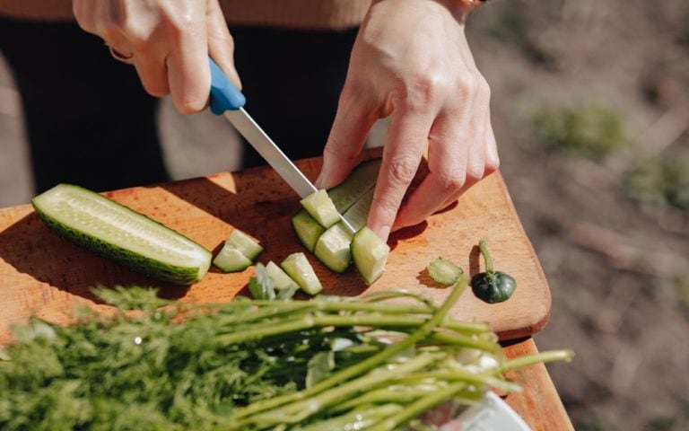 Girl slices vegetables on the board and prepares a salad on the nature